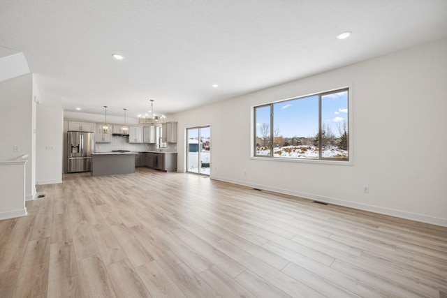 unfurnished living room with visible vents, recessed lighting, an inviting chandelier, light wood finished floors, and baseboards