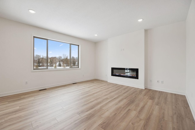 unfurnished living room featuring recessed lighting, baseboards, a glass covered fireplace, and light wood finished floors