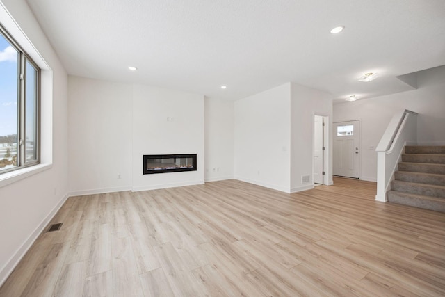 unfurnished living room featuring visible vents, recessed lighting, stairs, a glass covered fireplace, and light wood-type flooring