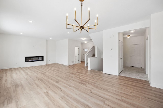 unfurnished living room featuring baseboards, recessed lighting, light wood-style floors, a glass covered fireplace, and a notable chandelier