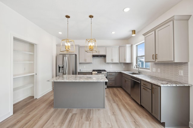 kitchen with a sink, stainless steel appliances, light wood-style floors, under cabinet range hood, and a center island