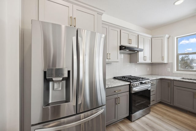 kitchen featuring gray cabinets, under cabinet range hood, appliances with stainless steel finishes, light wood-type flooring, and backsplash