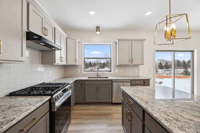 kitchen featuring light wood finished floors, under cabinet range hood, a notable chandelier, stainless steel appliances, and a sink