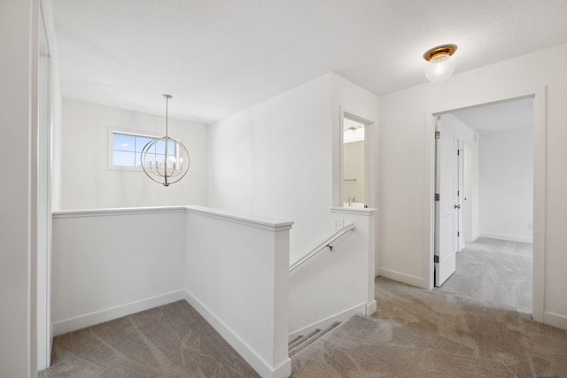 hall with baseboards, a textured ceiling, carpet flooring, a notable chandelier, and an upstairs landing