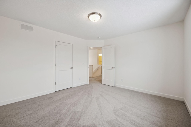 spare room with visible vents, a textured ceiling, carpet, and baseboards