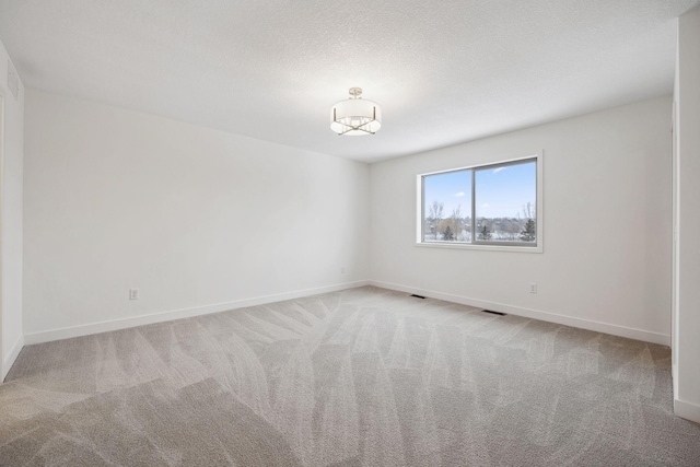 carpeted spare room with visible vents, baseboards, and a textured ceiling