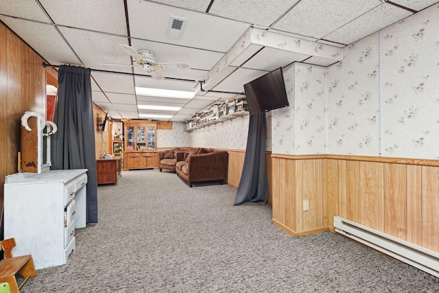 basement with a drop ceiling, carpet floors, a baseboard radiator, and ceiling fan