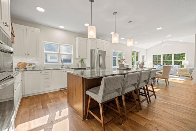 kitchen featuring stainless steel refrigerator, a wealth of natural light, a center island, and vaulted ceiling