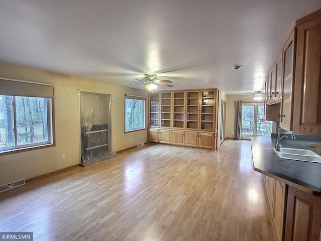 unfurnished living room featuring light hardwood / wood-style floors, ceiling fan, and sink