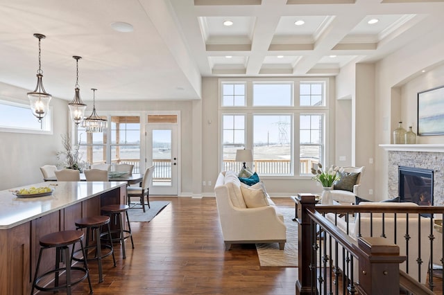 living room with coffered ceiling, a stone fireplace, beam ceiling, dark wood-type flooring, and crown molding