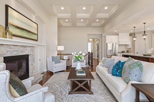 living room featuring hardwood / wood-style floors, beam ceiling, ornamental molding, a fireplace, and coffered ceiling