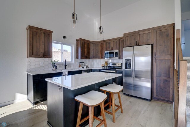 kitchen with light wood finished floors, stainless steel appliances, light countertops, decorative backsplash, and a kitchen bar