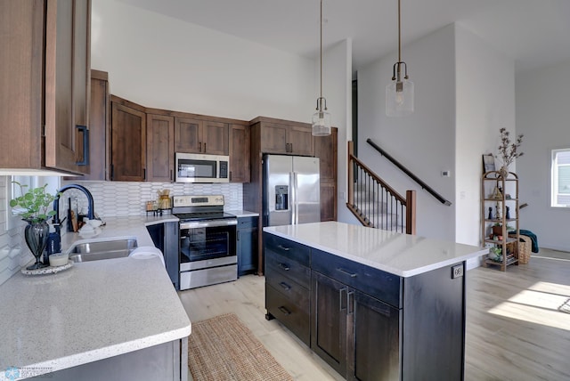 kitchen featuring light wood finished floors, tasteful backsplash, a high ceiling, stainless steel appliances, and a sink