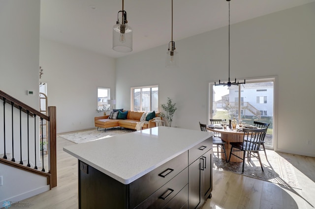 kitchen with a towering ceiling, light wood-style floors, light countertops, and hanging light fixtures