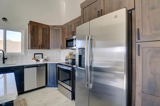 kitchen featuring light stone counters, backsplash, light wood-style flooring, appliances with stainless steel finishes, and a sink