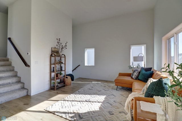 living area with high vaulted ceiling, stairs, baseboards, and wood finished floors