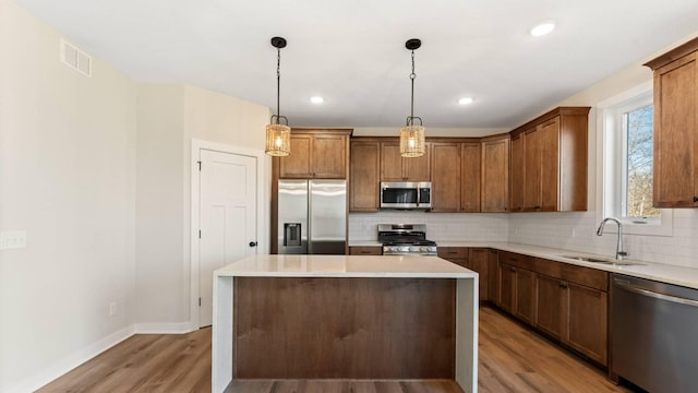 kitchen featuring a center island, decorative light fixtures, light hardwood / wood-style floors, appliances with stainless steel finishes, and sink