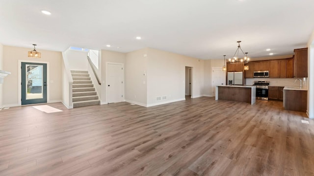 unfurnished living room featuring a notable chandelier, sink, and hardwood / wood-style flooring