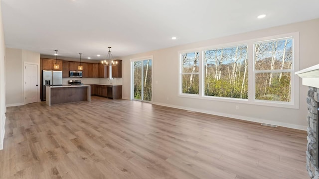 unfurnished living room with light hardwood / wood-style floors, a notable chandelier, and a stone fireplace