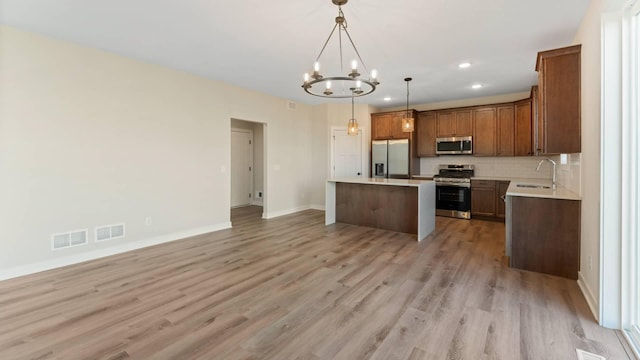 kitchen featuring stainless steel appliances, hanging light fixtures, a notable chandelier, a kitchen island, and sink