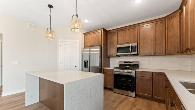 kitchen with a center island, hanging light fixtures, stainless steel appliances, light hardwood / wood-style floors, and decorative backsplash