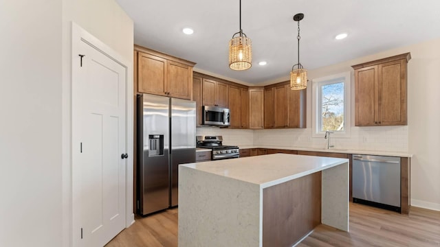 kitchen featuring appliances with stainless steel finishes, hanging light fixtures, light hardwood / wood-style floors, a center island, and sink