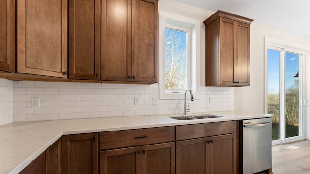 kitchen with light stone countertops, dishwasher, decorative backsplash, light wood-type flooring, and sink