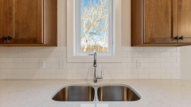 room details featuring sink, decorative backsplash, and light stone countertops