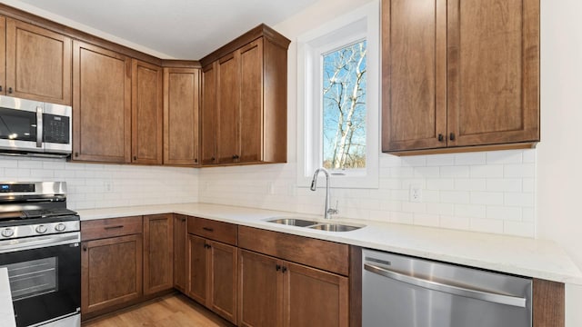 kitchen featuring stainless steel appliances, light wood-type flooring, backsplash, and sink