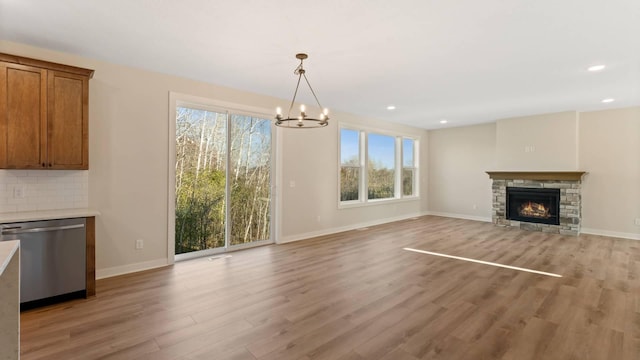 unfurnished living room featuring light hardwood / wood-style floors, a chandelier, and a stone fireplace