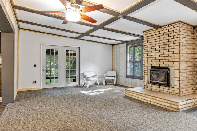 unfurnished living room featuring carpet, beam ceiling, a wood stove, and ceiling fan