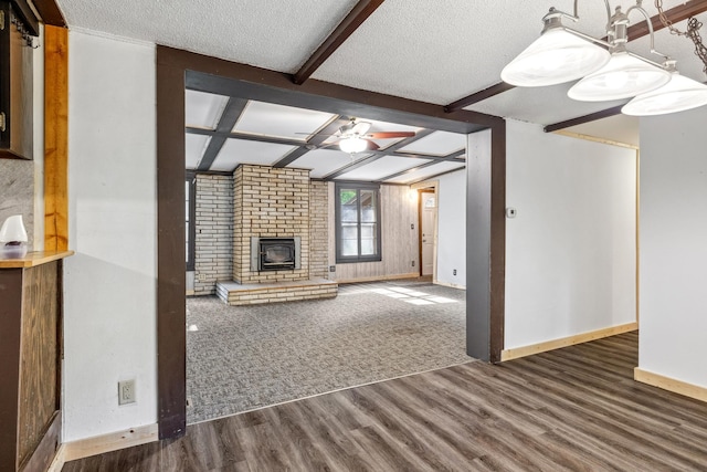 unfurnished living room featuring a textured ceiling, ceiling fan, beamed ceiling, a fireplace, and dark hardwood / wood-style floors