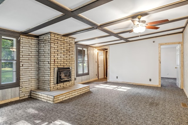 unfurnished living room with a wood stove, ceiling fan, beamed ceiling, and carpet