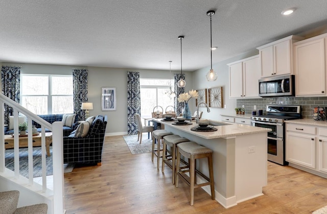 kitchen with appliances with stainless steel finishes, light hardwood / wood-style floors, a center island with sink, and sink