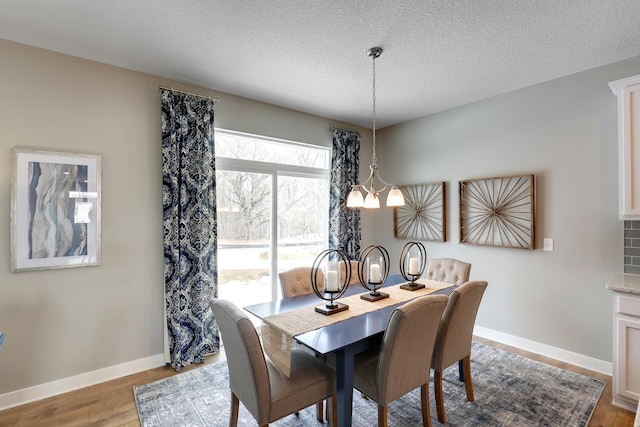 dining space with light hardwood / wood-style floors, a textured ceiling, and a chandelier