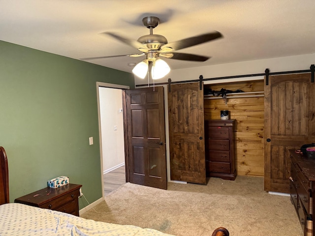 carpeted bedroom with wood walls, a barn door, and ceiling fan