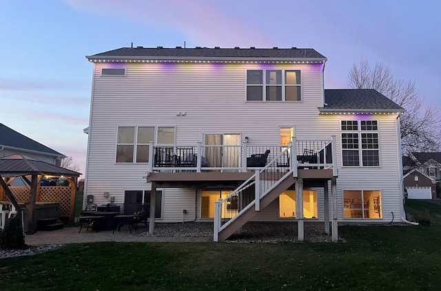 back house at dusk with a wooden deck, a gazebo, a lawn, and a patio