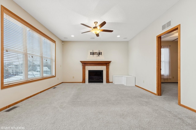 unfurnished living room with ceiling fan, plenty of natural light, carpet flooring, and a tile fireplace