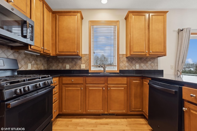 kitchen featuring a wealth of natural light, light hardwood / wood-style floors, sink, and black appliances