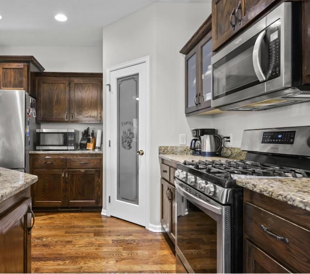 kitchen featuring stainless steel appliances, dark hardwood / wood-style floors, dark brown cabinetry, and light stone counters