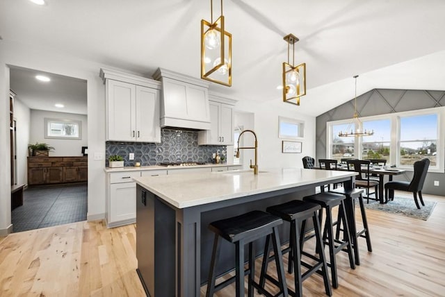 kitchen featuring sink, hanging light fixtures, gas cooktop, an island with sink, and vaulted ceiling