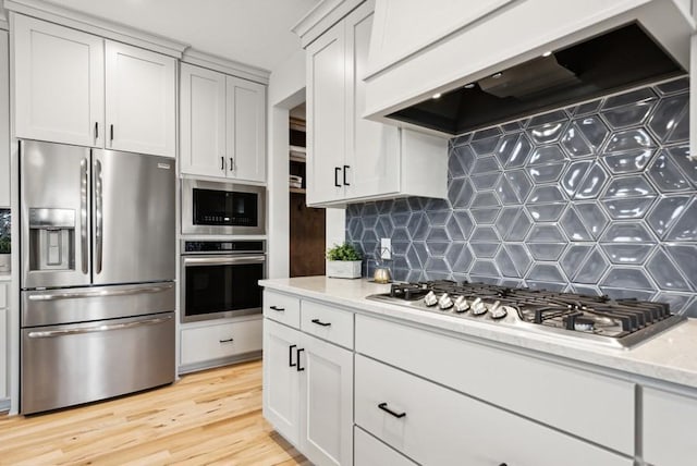 kitchen featuring tasteful backsplash, light hardwood / wood-style floors, light stone counters, custom range hood, and stainless steel appliances