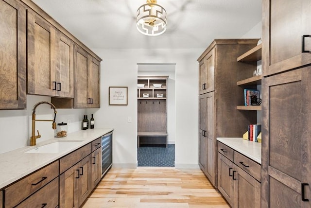 kitchen featuring light wood-type flooring, light stone countertops, sink, and beverage cooler