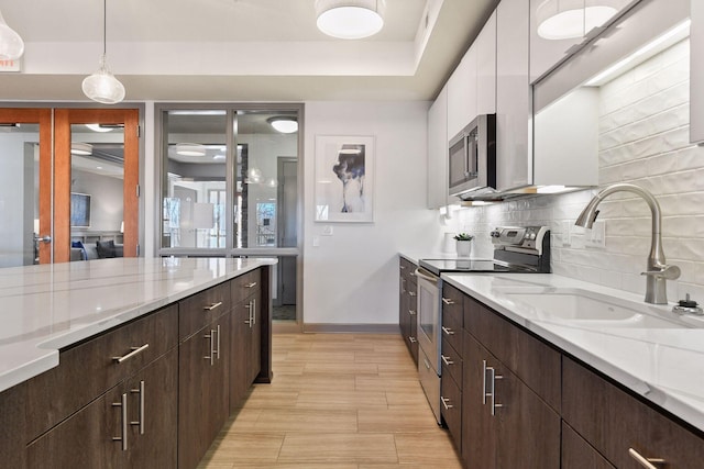 kitchen featuring white cabinets, sink, pendant lighting, light wood-type flooring, and appliances with stainless steel finishes