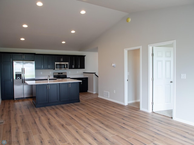 kitchen with high vaulted ceiling, a center island with sink, sink, wood-type flooring, and stainless steel appliances