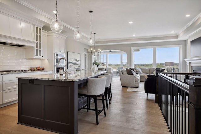 kitchen featuring light stone countertops, wood-type flooring, an island with sink, a kitchen bar, and white cabinetry