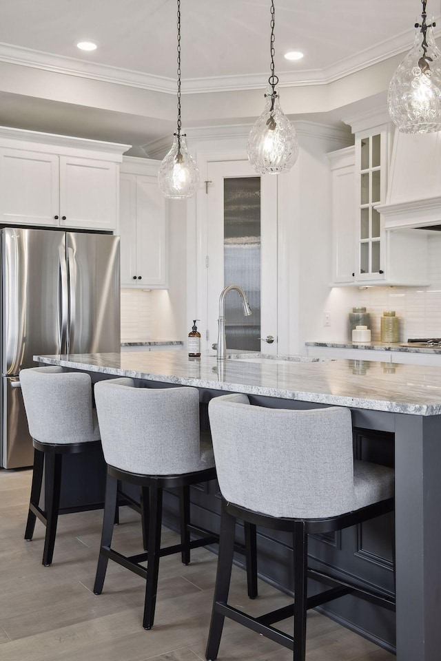 kitchen featuring stainless steel fridge, tasteful backsplash, hanging light fixtures, white cabinetry, and crown molding