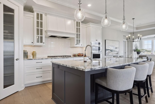 kitchen with a kitchen island with sink, light hardwood / wood-style flooring, pendant lighting, and white cabinets