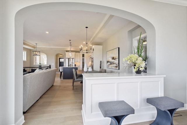 kitchen with crown molding, a notable chandelier, pendant lighting, light wood-type flooring, and white cabinets