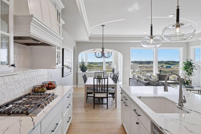 9155 Mills Dr, Chanhassen, MN 55317 - kitchen featuring stainless steel gas stovetop, a sink, custom range hood, light wood-style floors, and tasteful backsplash